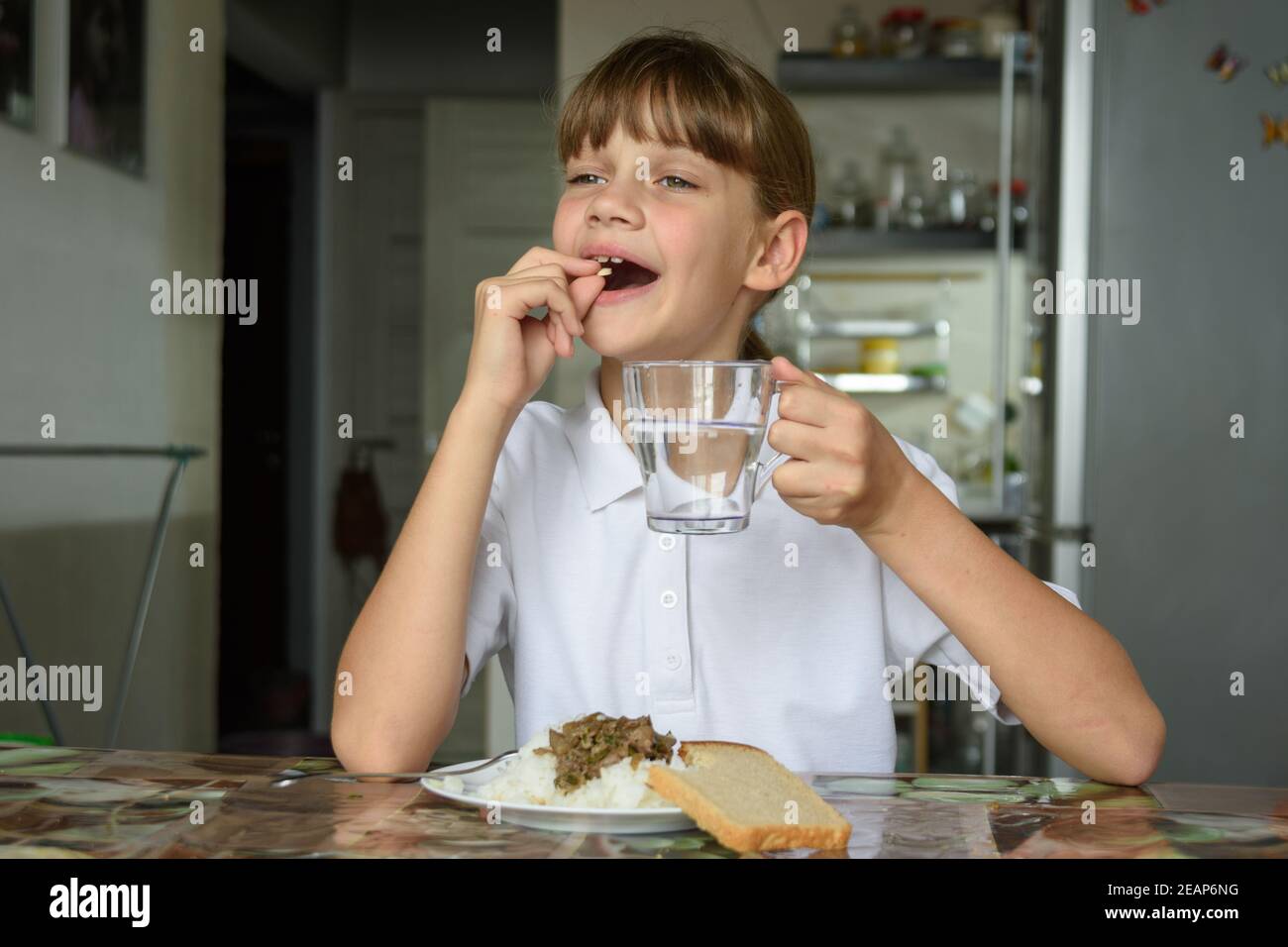 Glückliches kleines Mädchen, das vor dem Essen eine Pille trinkt Stockfoto