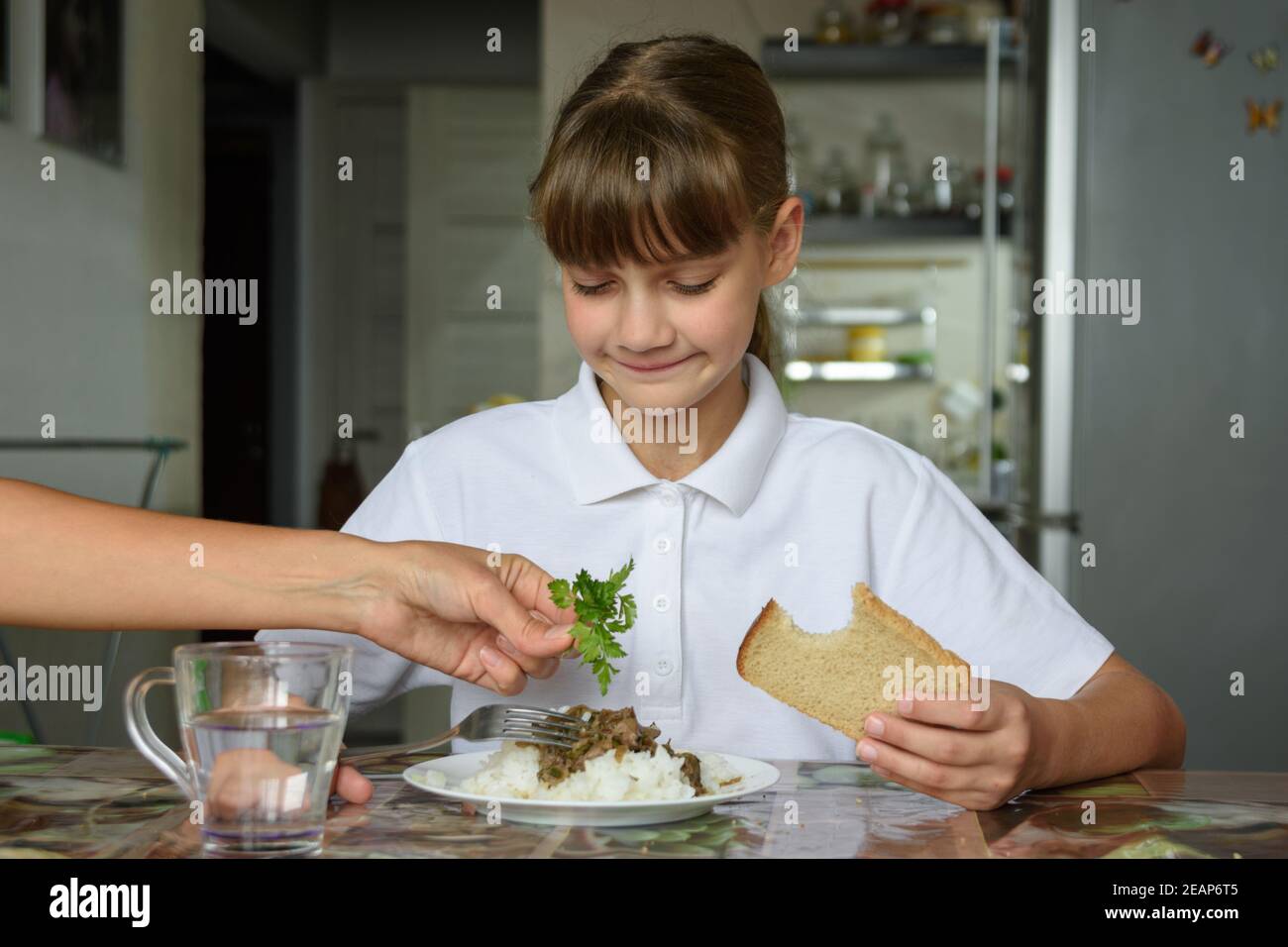 Mama fügt frische Kräuter auf den Teller ihrer Tochter, Tochter-Dines Stockfoto