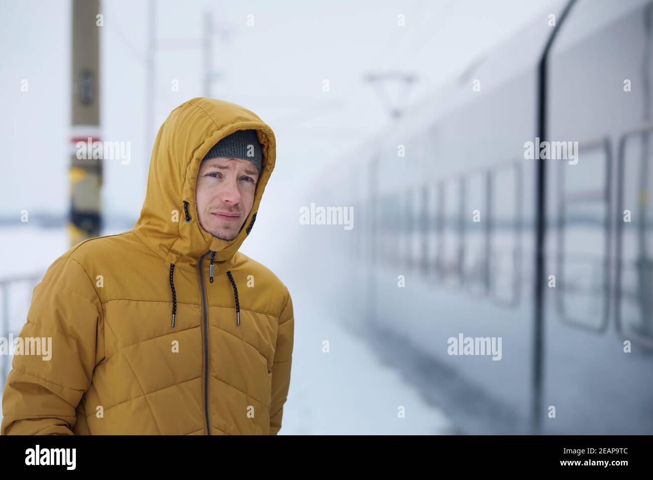 Der junge Mann fährt mit dem Zug während des frostigen Tages. Passagier auf Bahnsteig Bahnhof im Winter Tag. Stockfoto