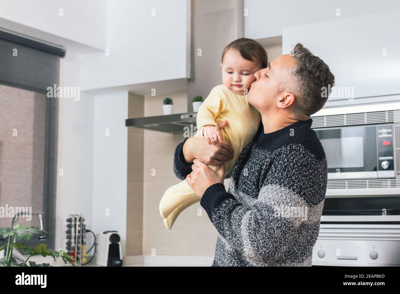 Stock Foto von jungen alleinerziehenden Vater küssen sein kleines Baby, während er ihn in den Armen. Mann und Kind, Eltern umarmen Kind zärtlichen Moment. Single Dad fa Stockfoto
