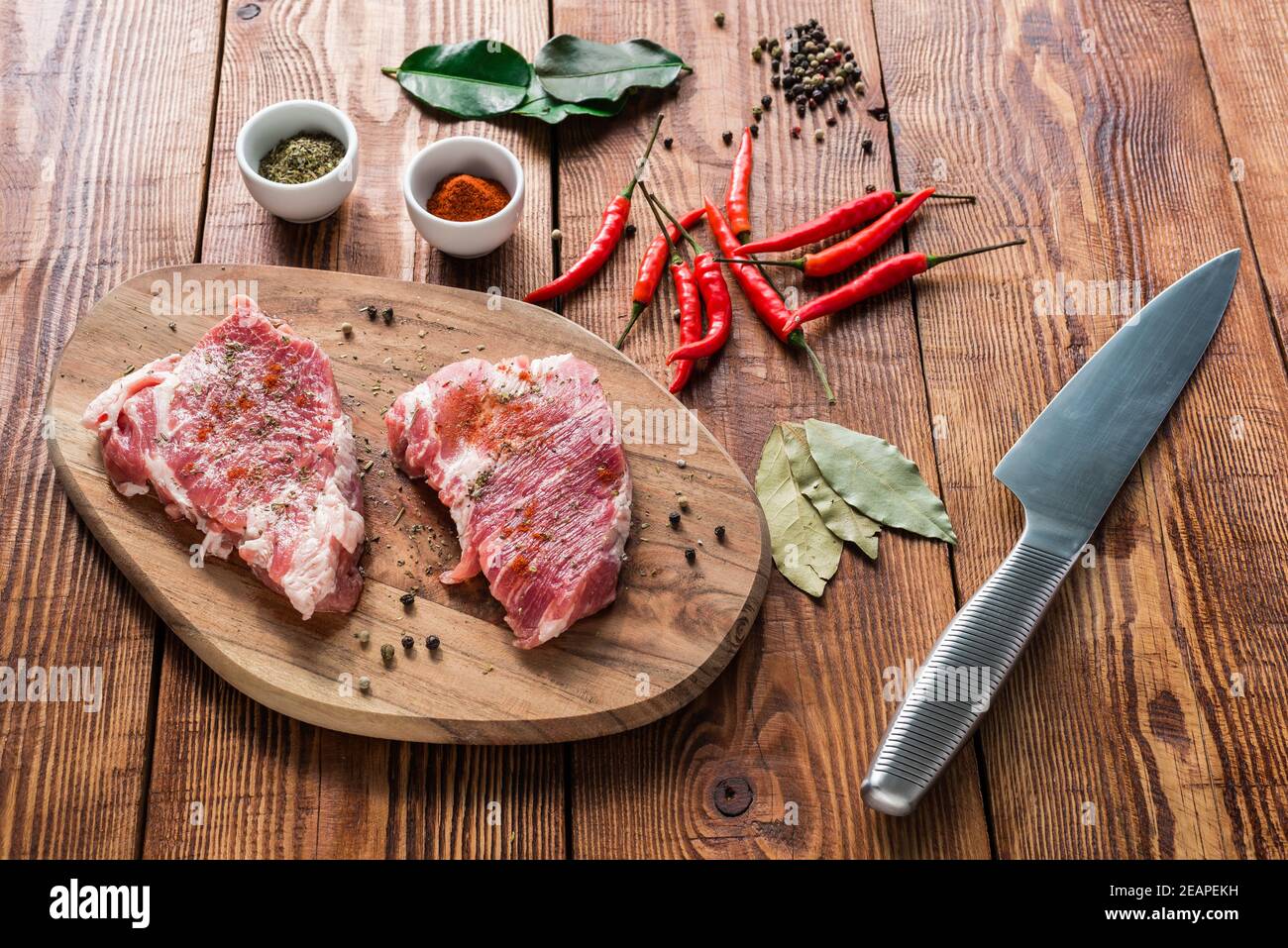 Rohe Steaks mit Gewürzen und Messer auf Holztisch. Stockfoto