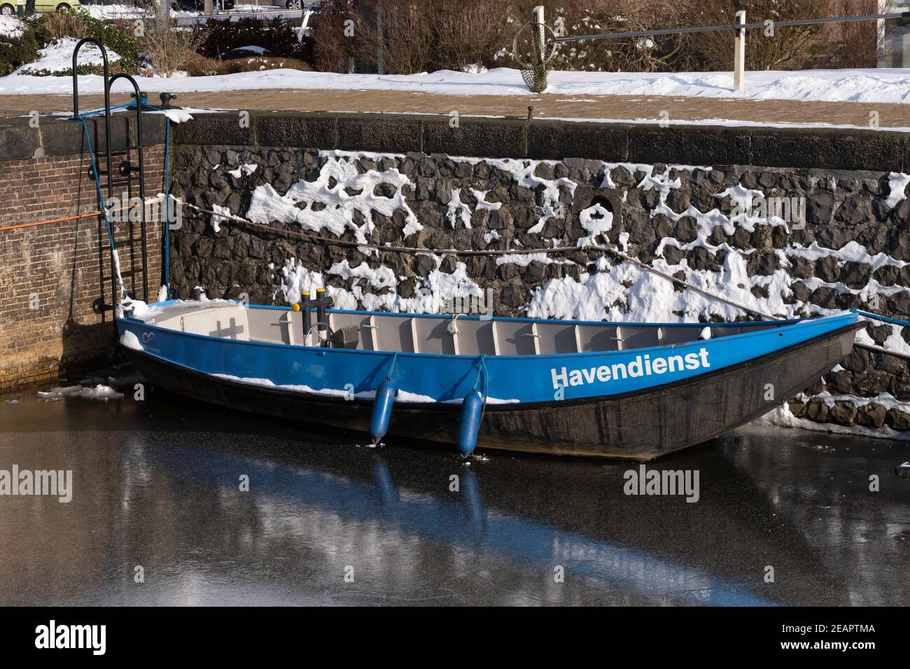 Eisenboot mit dem blauen Rand des Hafendienstes ('havendienst') ist im Eis gegen den Kai eingefroren Lemmer Stockfoto