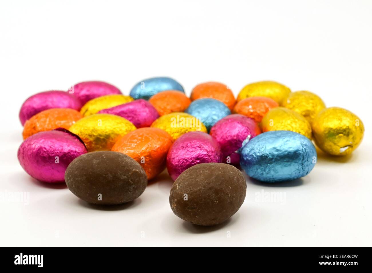 Kleine Schokoladen-Ostereier in farbigen Folienverpackungen auf einem schlichten Hintergrund. Keine Personen. Stockfoto