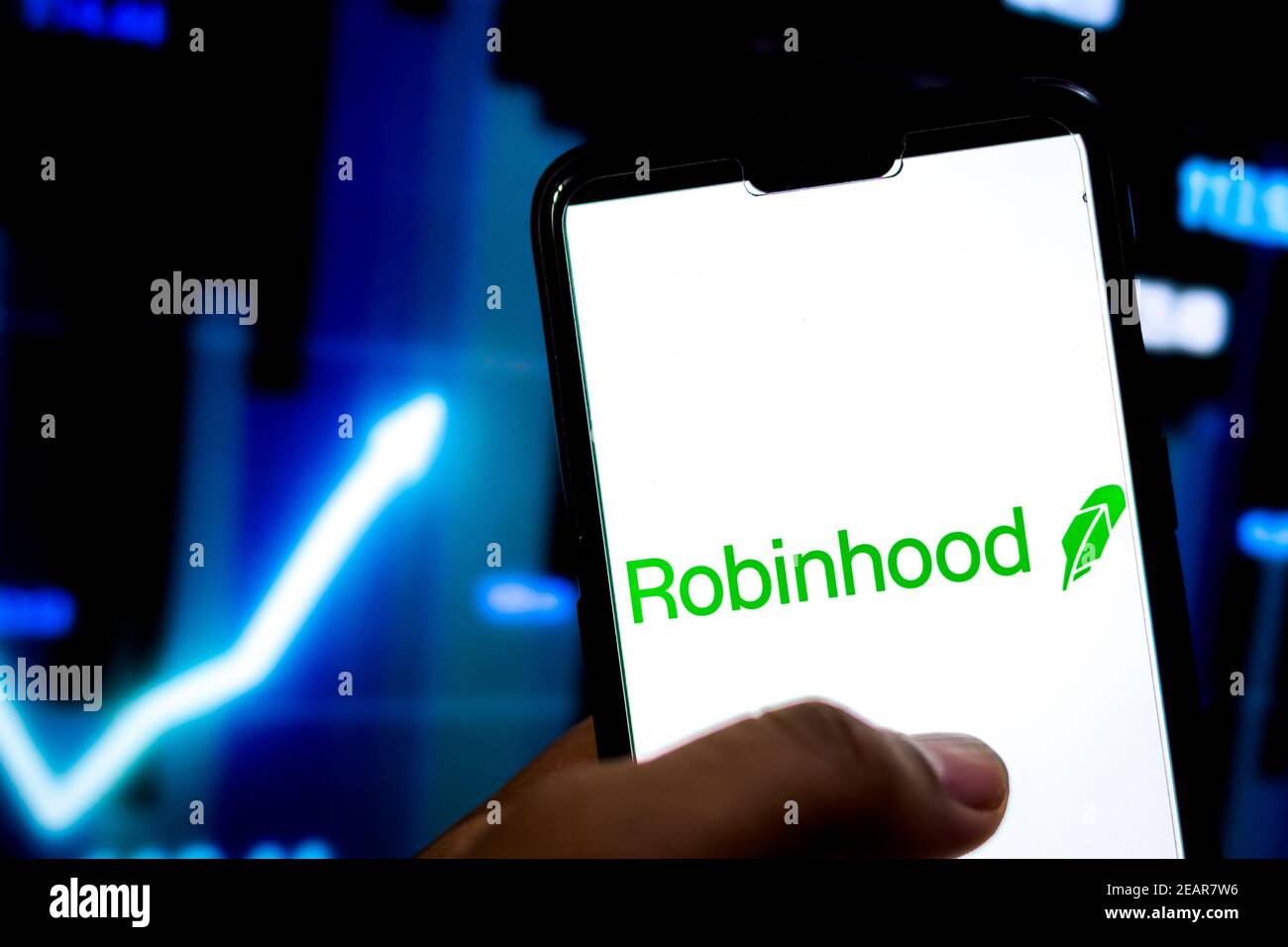Man hält Smartphone mit Robinhood-Anwendungslogo gegen die Börsenchart im Hintergrund. Stockfoto