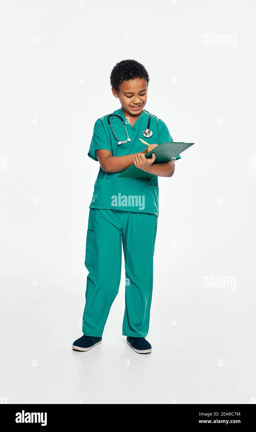 Junge spielt einen Arzt. Afroamerikanisches männliches Kind schreibt medizinische Behandlung auf seine Zwischenablage. Weißer Hintergrund Stockfoto