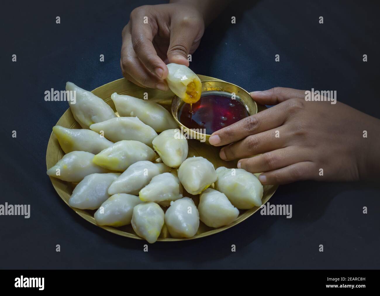 Köstliche bengalische Reismehl Kokosnussknödel serviert während bengali indian Festival von makar sankranti. Hände essen Knödel mit Dattelpalme Jaggery. Stockfoto