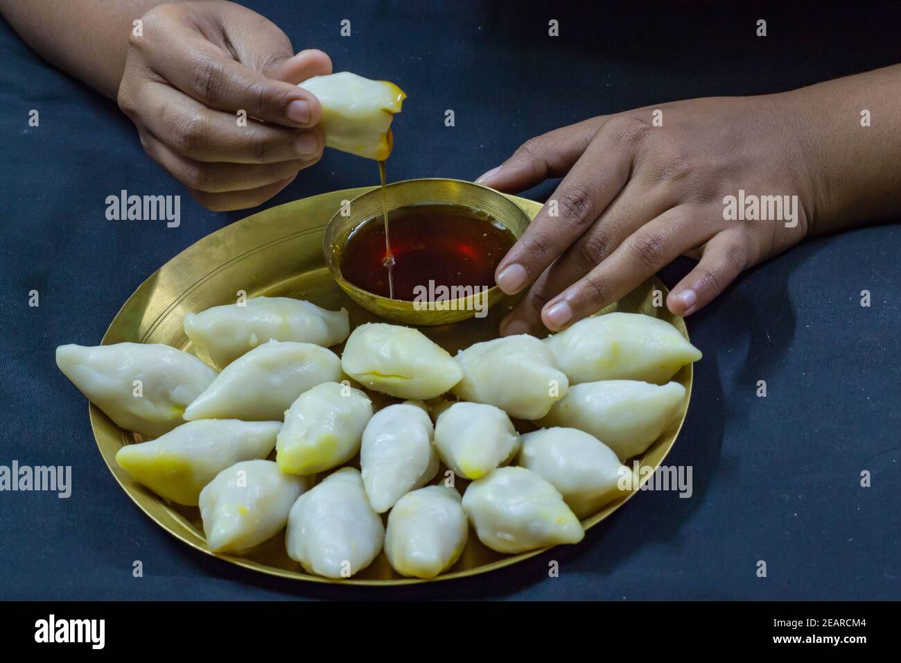 Köstliche bengalische Reismehl Kokosnussknödel serviert während bengali indian Festival von makar sankranti. Hände essen Knödel mit Dattelpalme Jaggery. Stockfoto