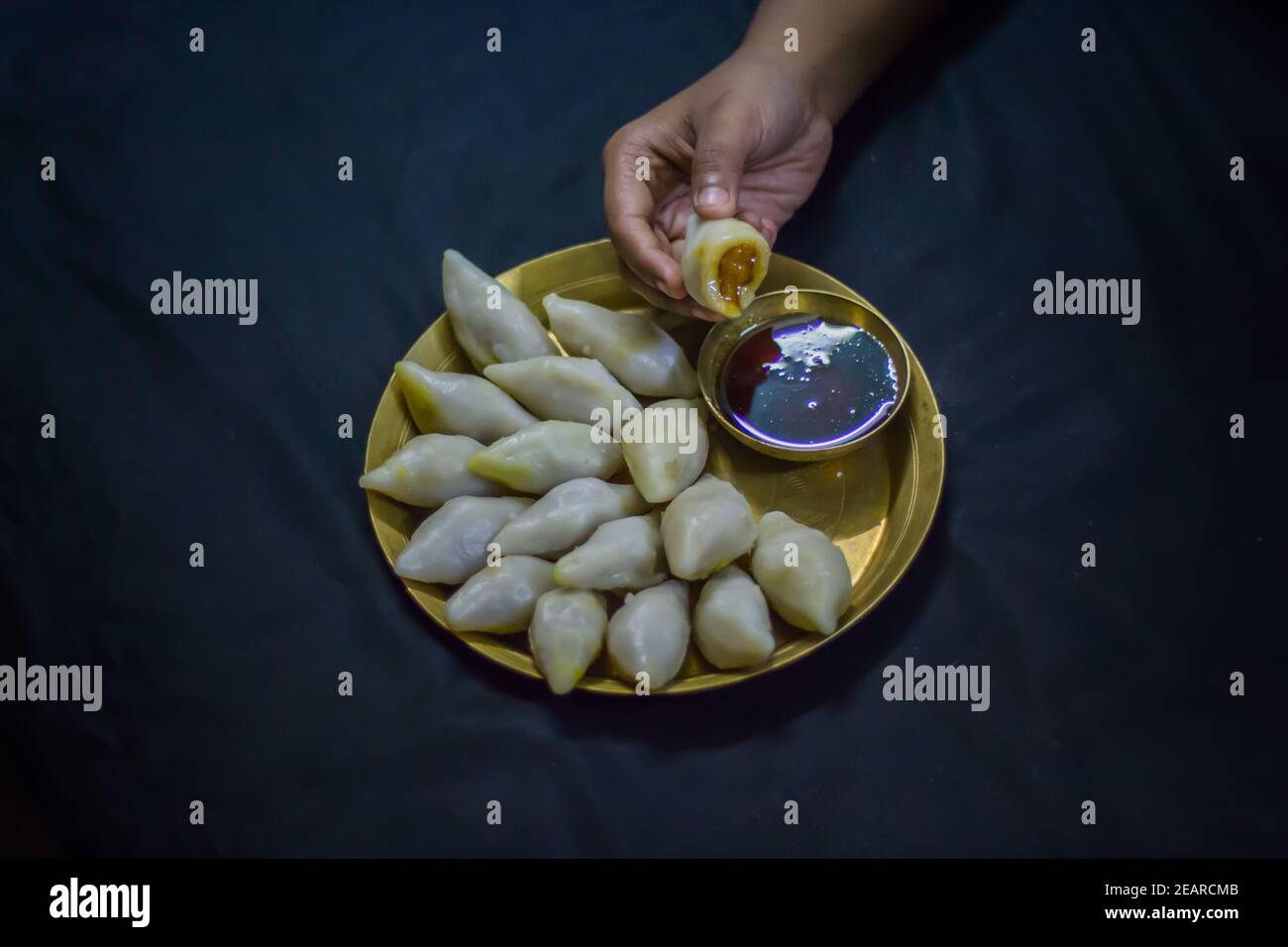 Köstliche bengalische Reismehl Kokosnussknödel serviert während bengali indian Festival von makar sankranti. Hände essen Knödel mit Dattelpalme Jaggery. Stockfoto