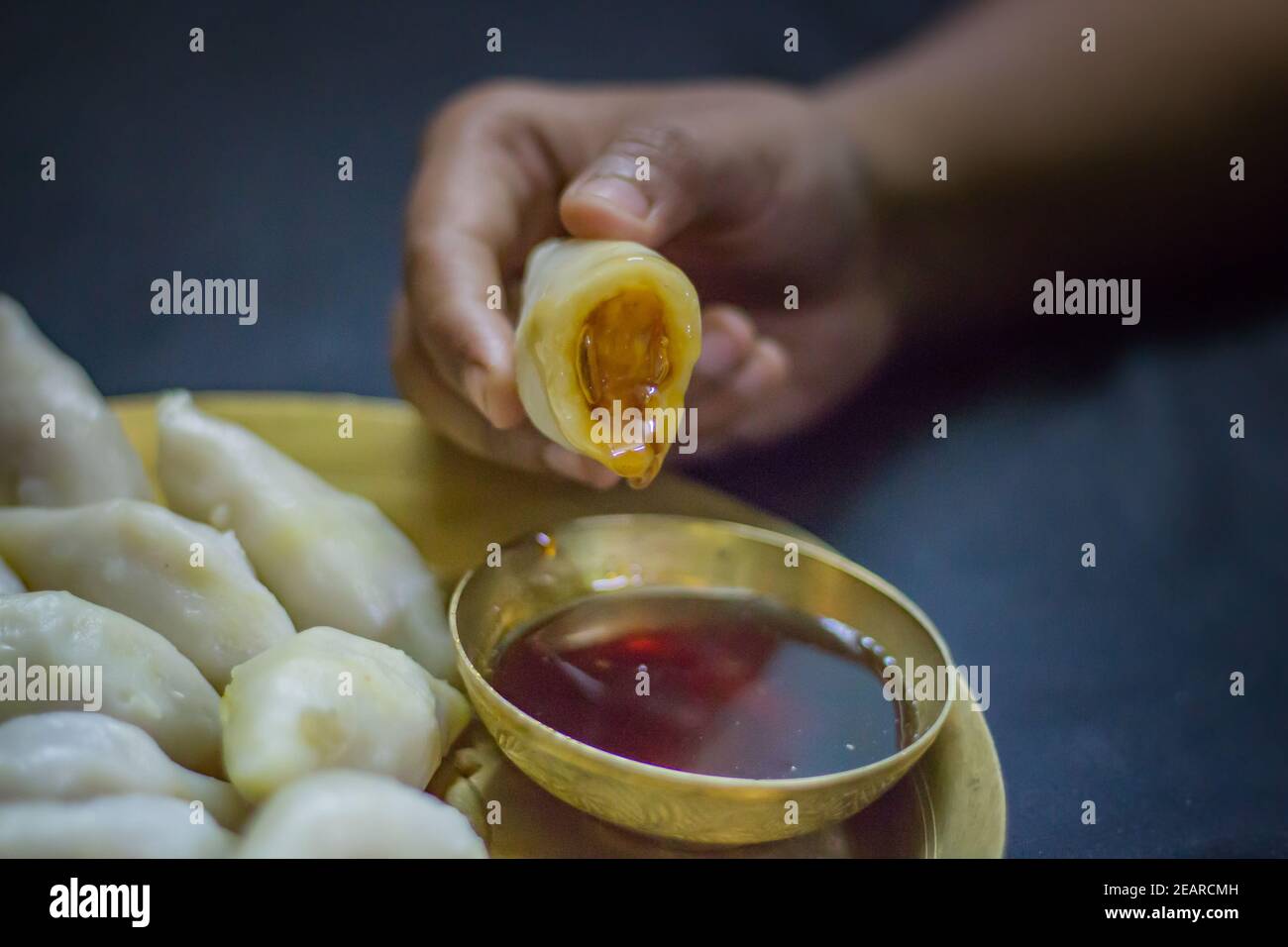 Köstliche bengalische Reismehl Kokosnussknödel serviert während bengali indian Festival von makar sankranti. Hände essen Knödel mit Dattelpalme Jaggery. Stockfoto