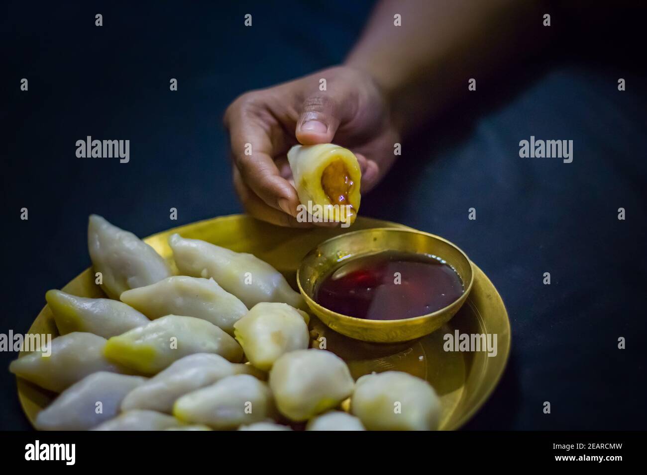 Köstliche bengalische Reismehl Kokosnussknödel serviert während bengali indian Festival von makar sankranti. Hände essen Knödel mit Dattelpalme Jaggery. Stockfoto