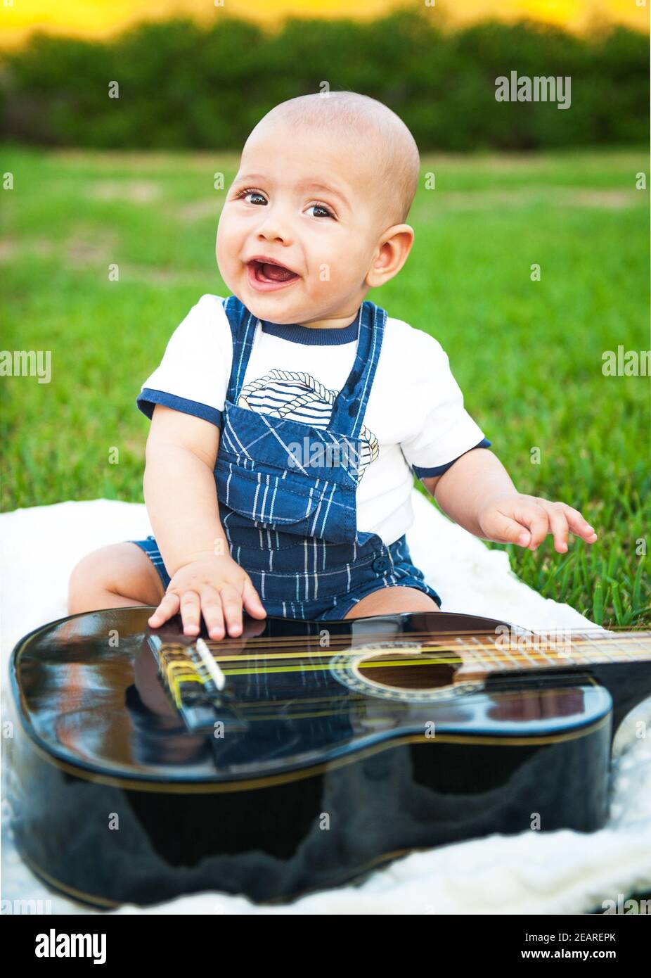 Der kleine Junge mit einer Gitarre auf dem Gras. Stockfoto