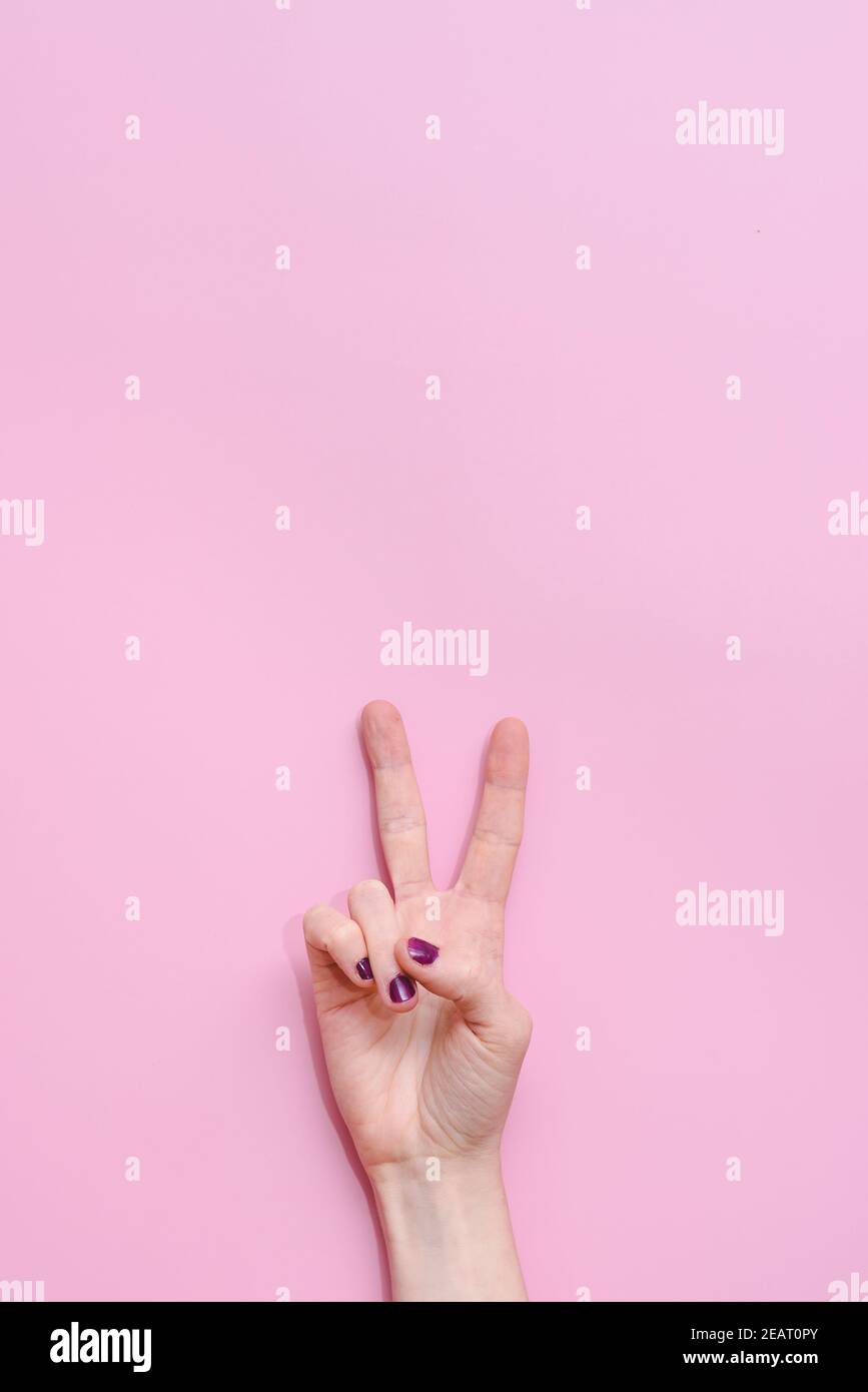Vertikale Übernahme der Finger einer kaukasischen jungen Frau Tun die Geste des Sieges mit rosa Hintergrund Konzept der Erfolg und Kampf gegen Krebs Stockfoto