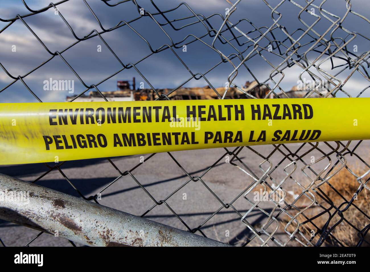 Warnband für Gefahren für die Umwelt und Gesundheit an einem verdrehten Kettengliederzaun. Stockfoto