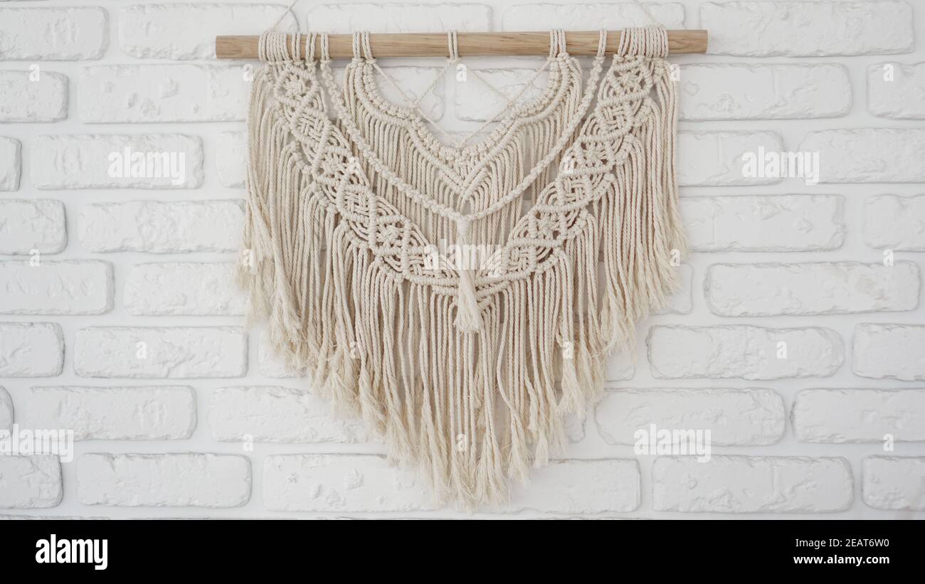 Wandpaneel im Stil von Boho aus Baumwollfäden in natürlicher Farbe auf einer weißen Ziegelwand. Schöne Boho Macrame Wandpaneel für eine gemütliche Atmosphäre Stockfoto