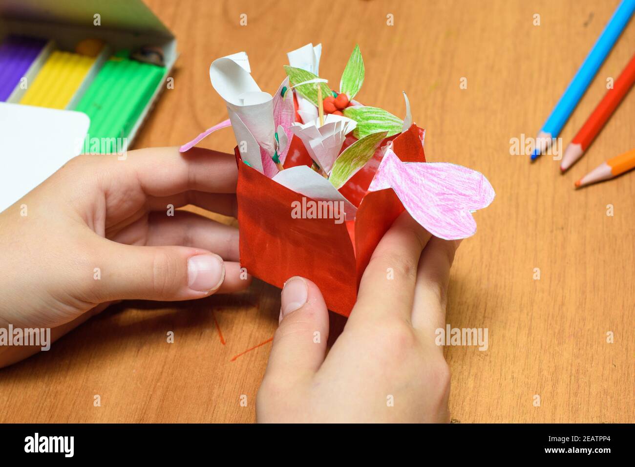 Ein Mädchen hält ein hausgemachtes Geschenk für Mama in ihren Händen, Schreibwaren auf dem Tisch im Hintergrund Stockfoto