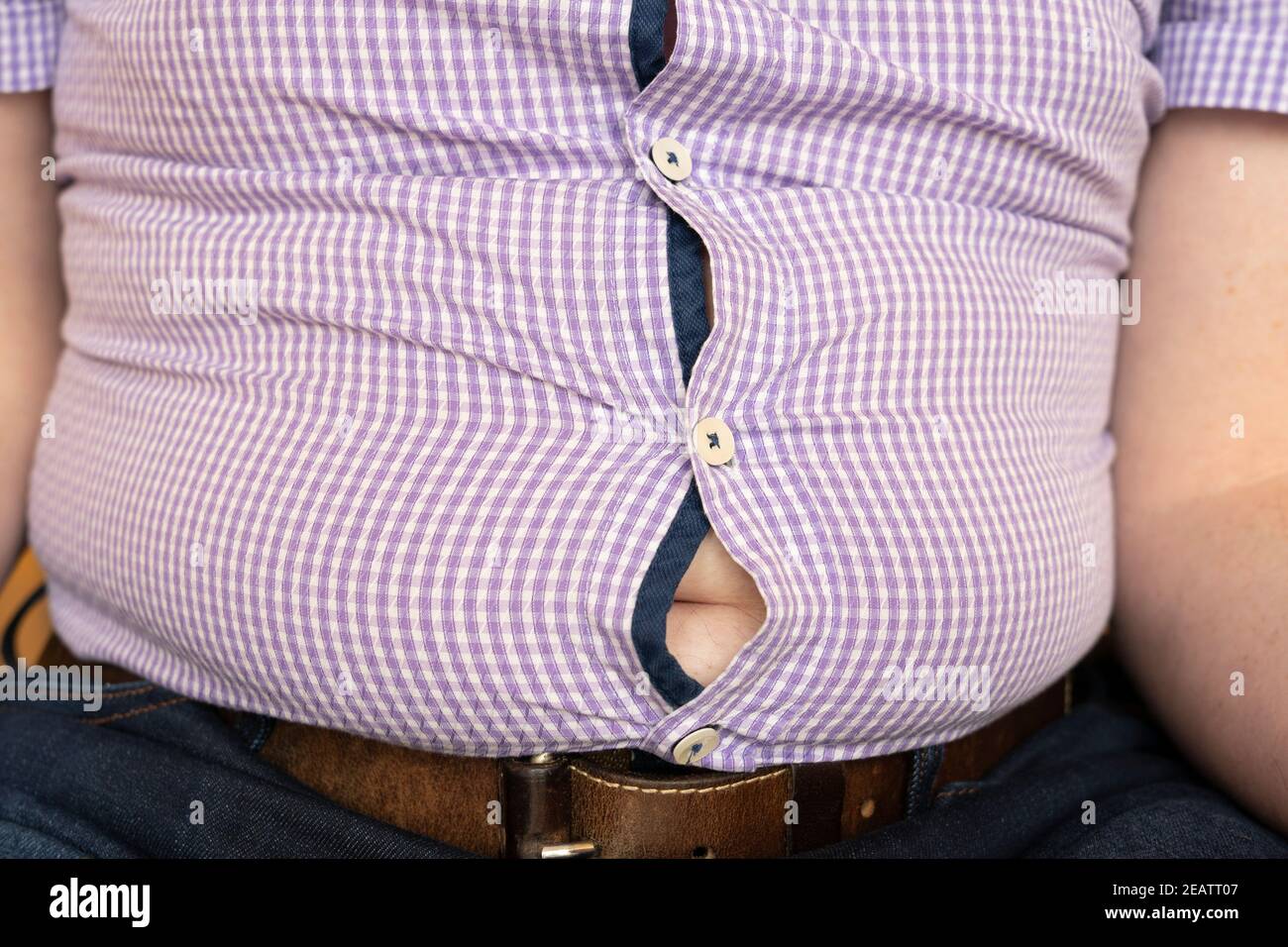 Ein übergewichtiger Mann mit einem Hemd, das über seinen großen Bauch gestreckt ist. Thema: Bierbauch, Übergewicht, covid-19 Lockdown, mangelnde Bewegung, sitzende Lebensweise Stockfoto
