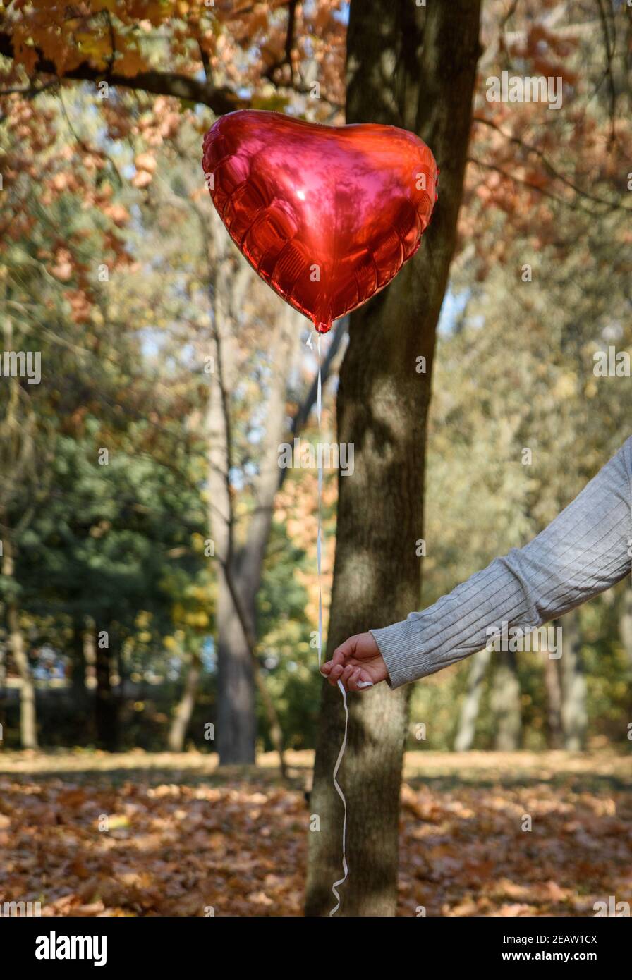 Weibliche Hand hält einen roten Ballon in Form von Ein Herz Stockfoto