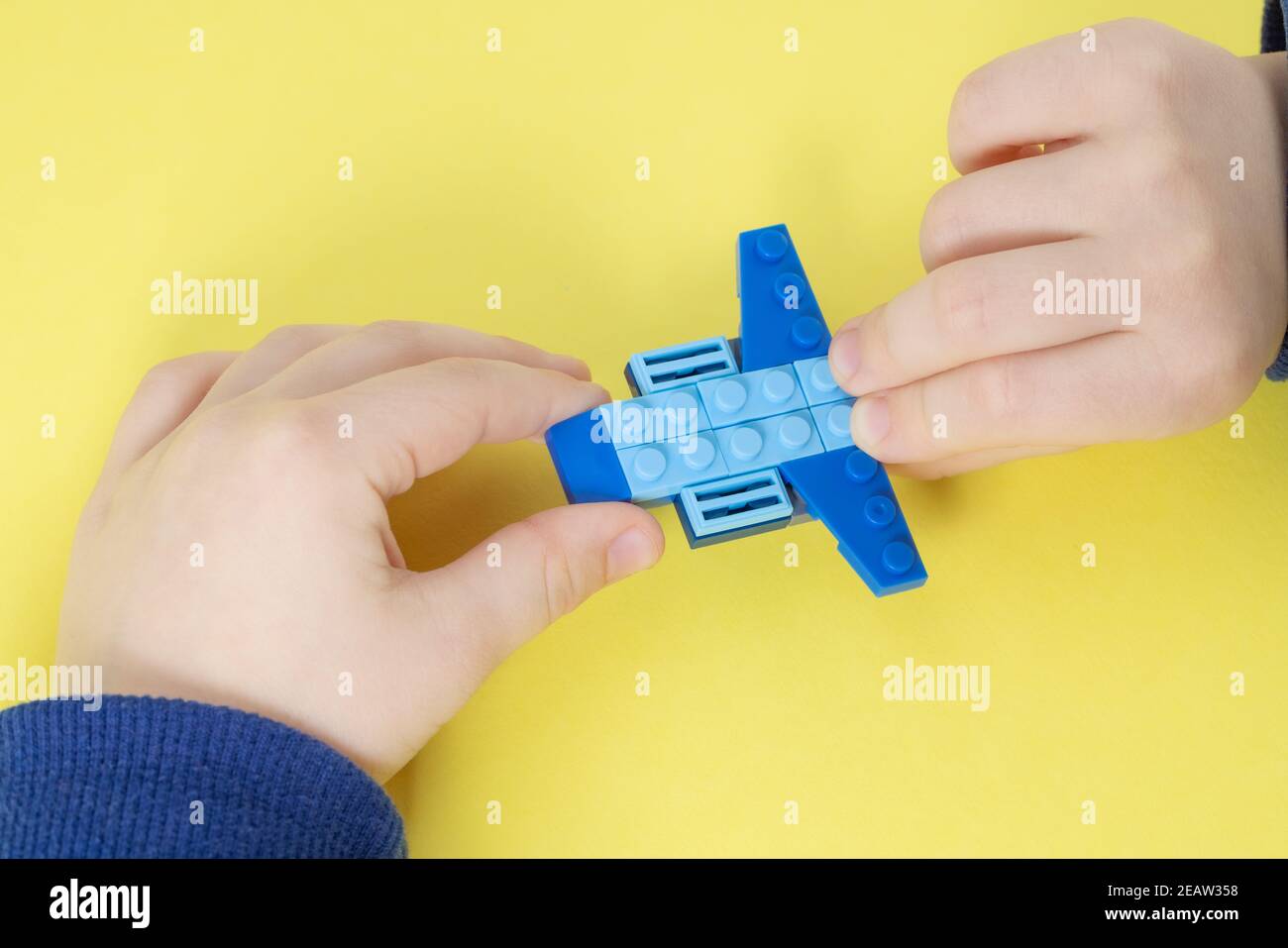 Kind spielt mit bunten Bauklötzen. Kinderhände mit Ziegeln Spielzeug auf gelbem Hintergrund. Lernspielzeug, flach liegend, Draufsicht. Stockfoto