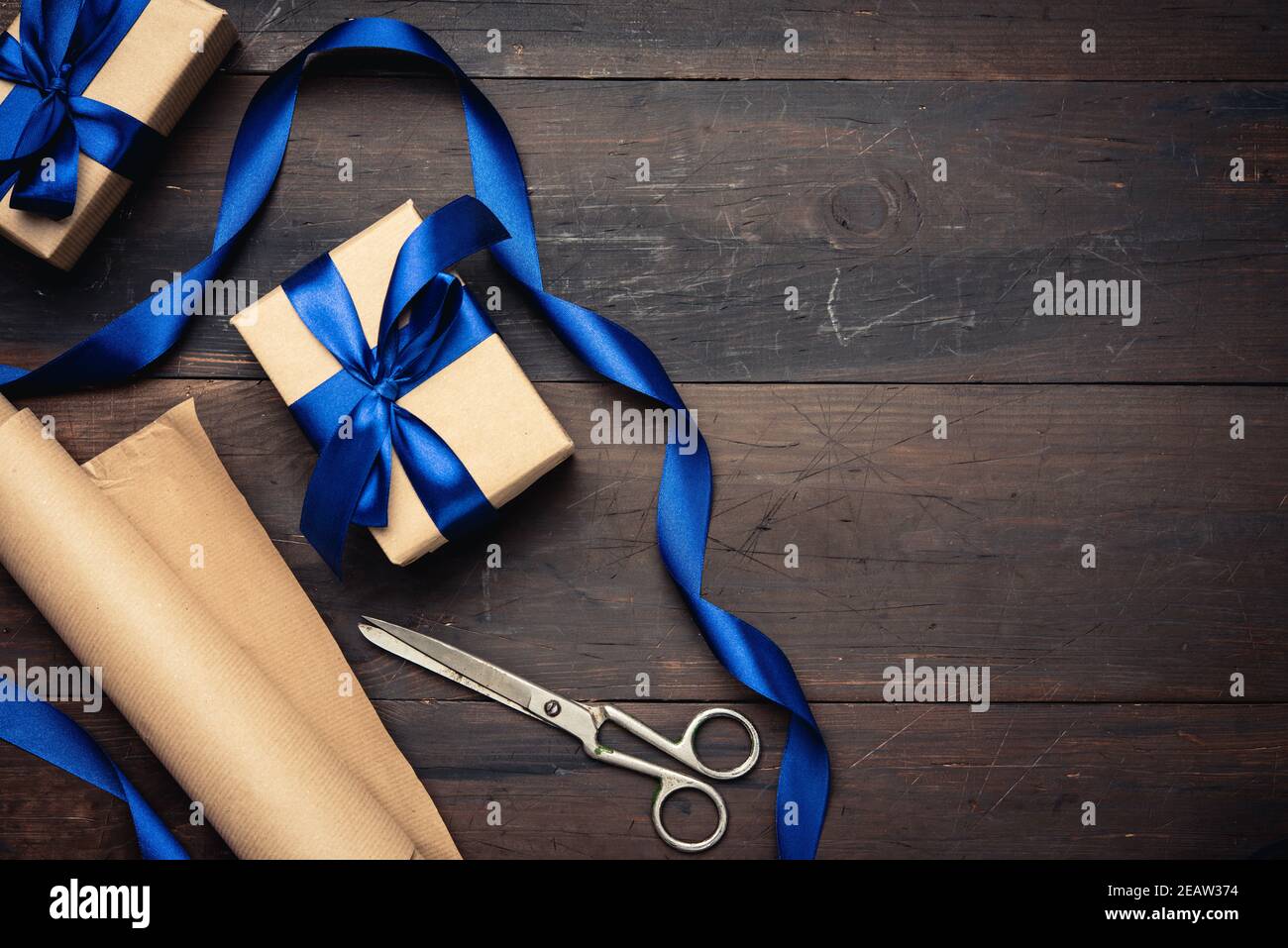 Box in braunem Papier verpackt und mit einem blauen Seidenband mit einer Schleife gebunden, Geschenk auf einem braunen Holzhintergrund Stockfoto