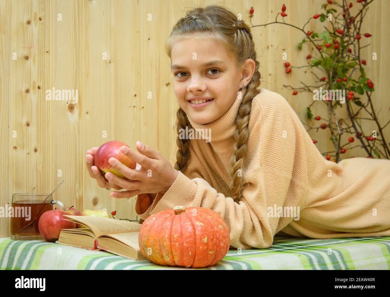 Ein Mädchen, das sich hinlegt, liest ein Buch, hält einen Apfel in der Hand und schaut glücklich in den Rahmen Stockfoto