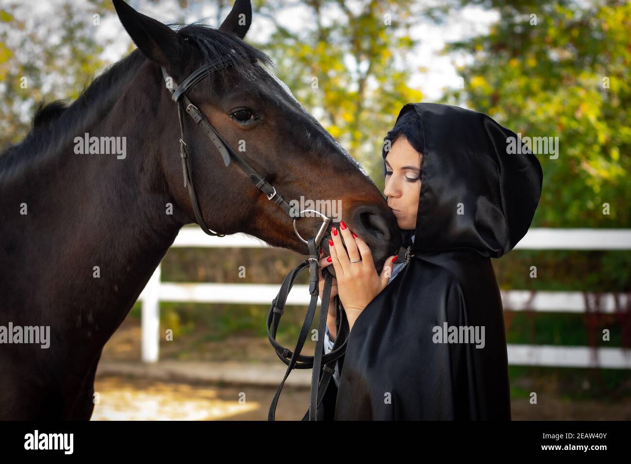 Mädchen in einem schwarzen Mantel umarmt und küsst ein Pferd Stockfoto