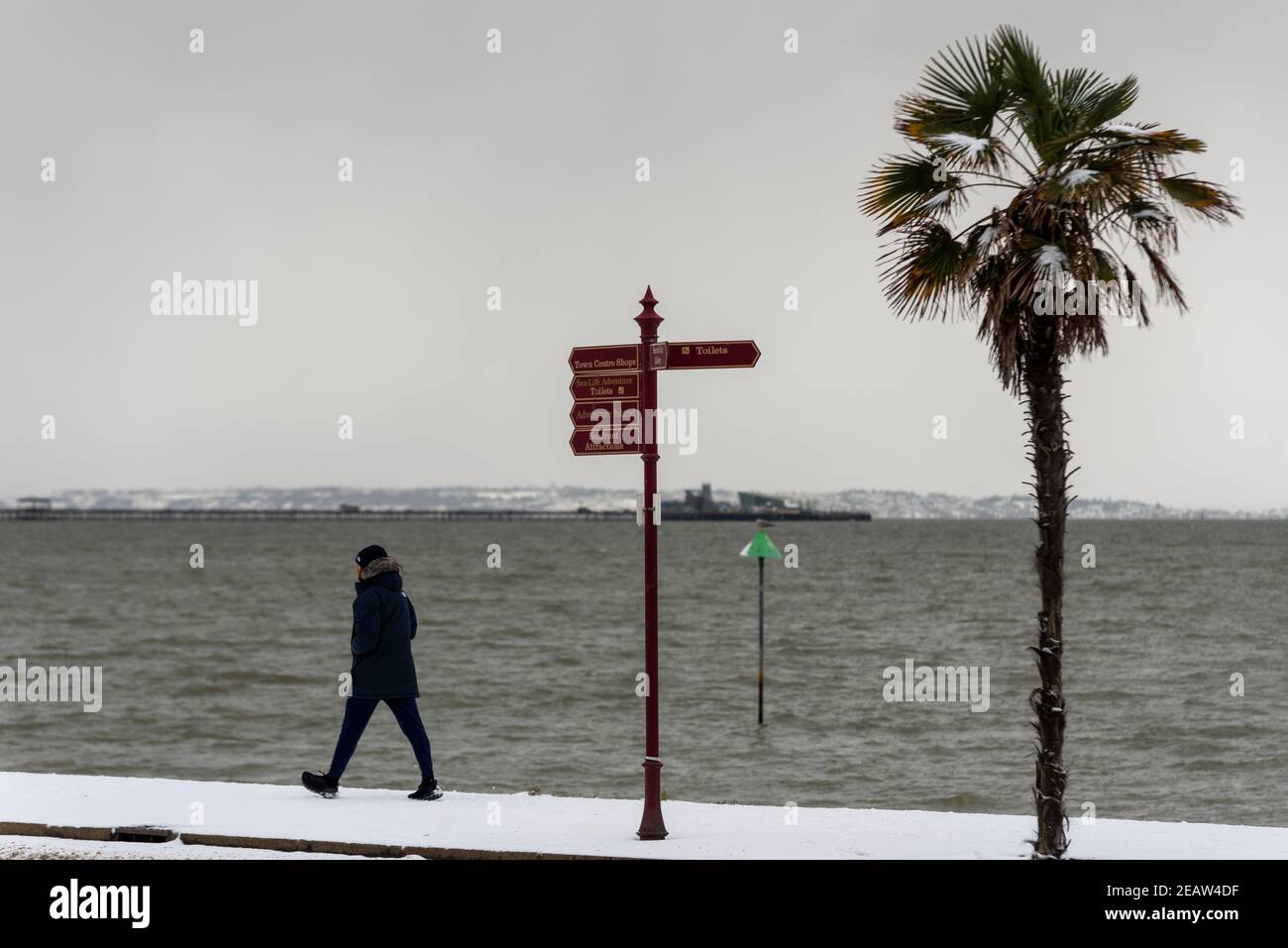 Männlicher Erwachsener, der entlang der Strandpromenade an der Themse-Mündung in Southend on Sea, Essex, Großbritannien, mit Schnee vom Storm Darcy geht. Winterbekleidung Stockfoto