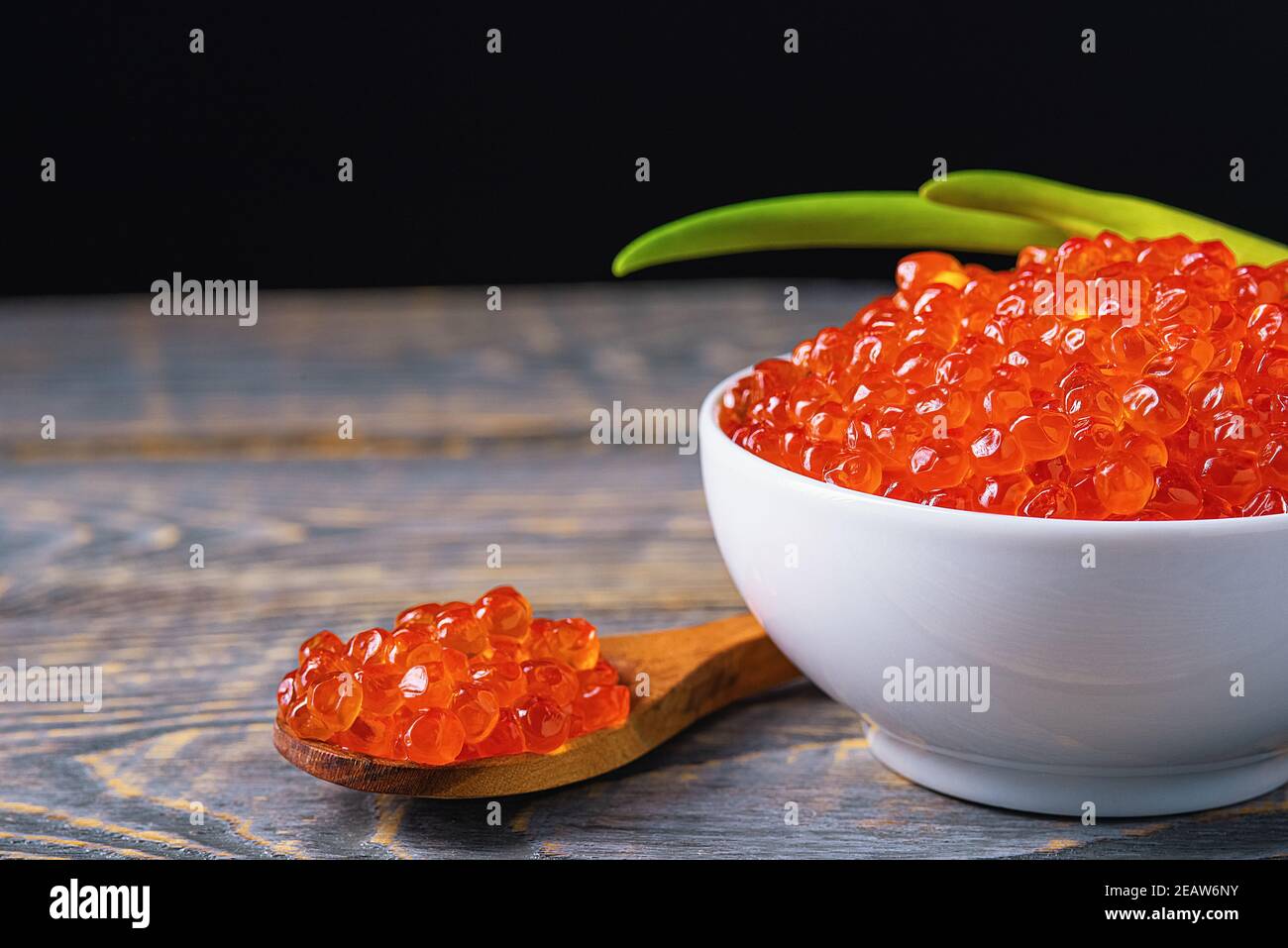 Roter Kaviar in einem Holzbecher auf einem Holzhintergrund mit einem Löffel. Stockfoto