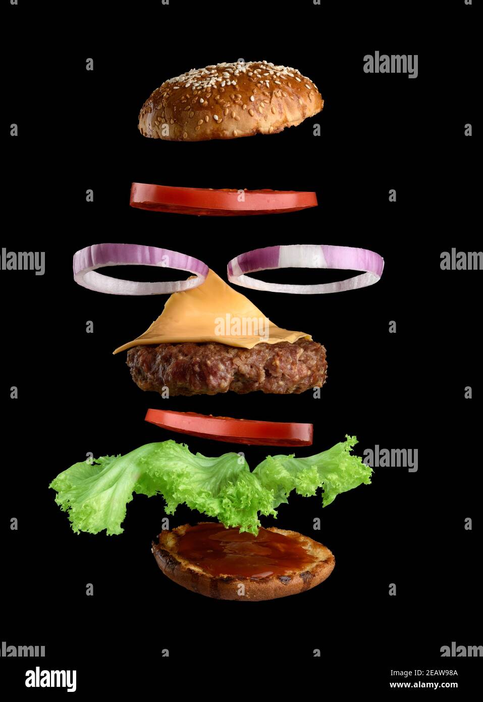 Fliegende Zutaten eines klassischen Cheeseburger Sesambrötchen, Zwiebelringe, Tomatenscheiben und einem saftigen Grillschnitzel Stockfoto