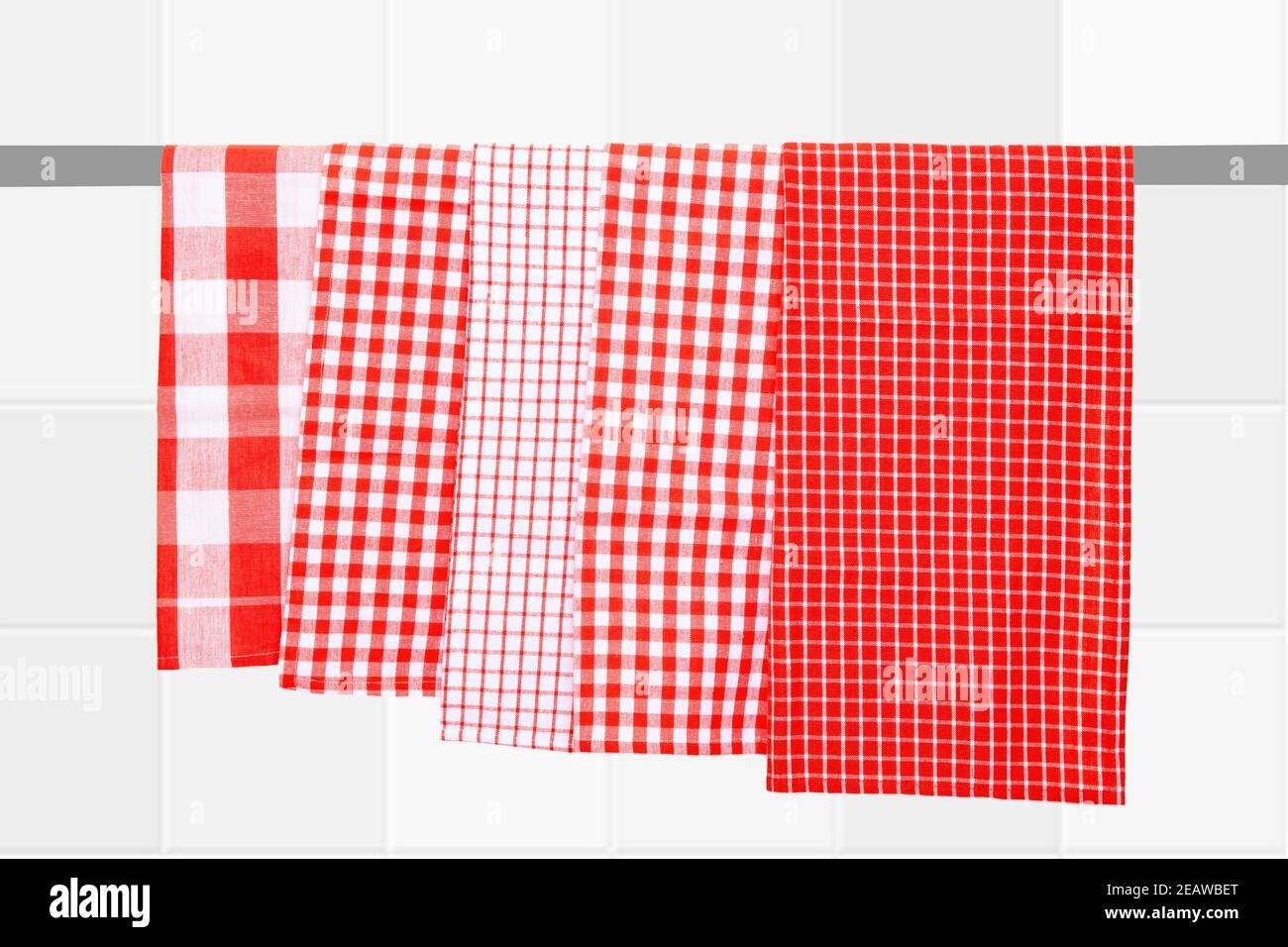 Nahaufnahme von verschiedenen rot karierten Küchentüchern hängen auf einer Kleiderstange vor verschwommenem hellen Fliesenhintergrund. Stockfoto