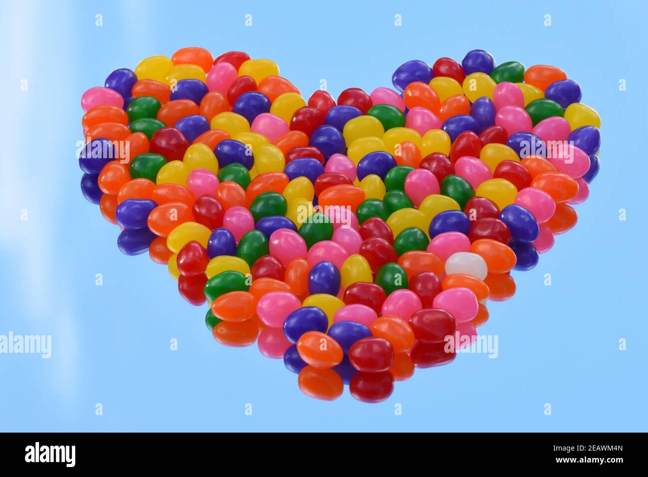 Herzförmige bunte Gelee Bohnen auf dem Spiegel mit der Reflexion des blauen Himmels Hintergrund. Speicherplatz kopieren. 3-dimensional. Stockfoto