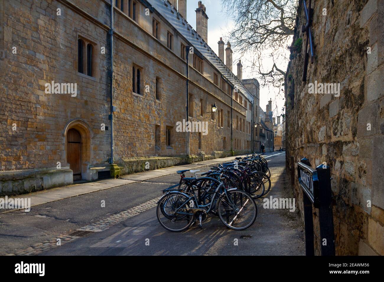 Brasenose Lane mit Abendlicht wirft diagonale Schatten entlang Steinmauer. Mit Fahrrädern, hölzernen Bogentüren und Laternen. Oxford University Stockfoto