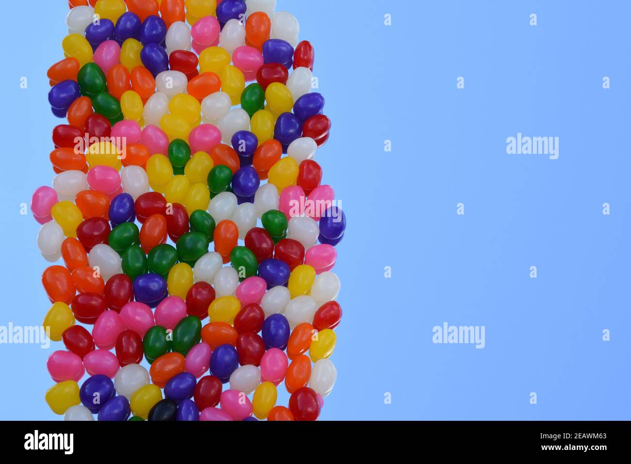 Mehrfarbige Jelly Bohnen in vertikaler Linie auf dem Spiegel mit der Reflexion des blauen Himmels Hintergrund. Draufsicht. Speicherplatz kopieren. 3-dimensional. Stockfoto