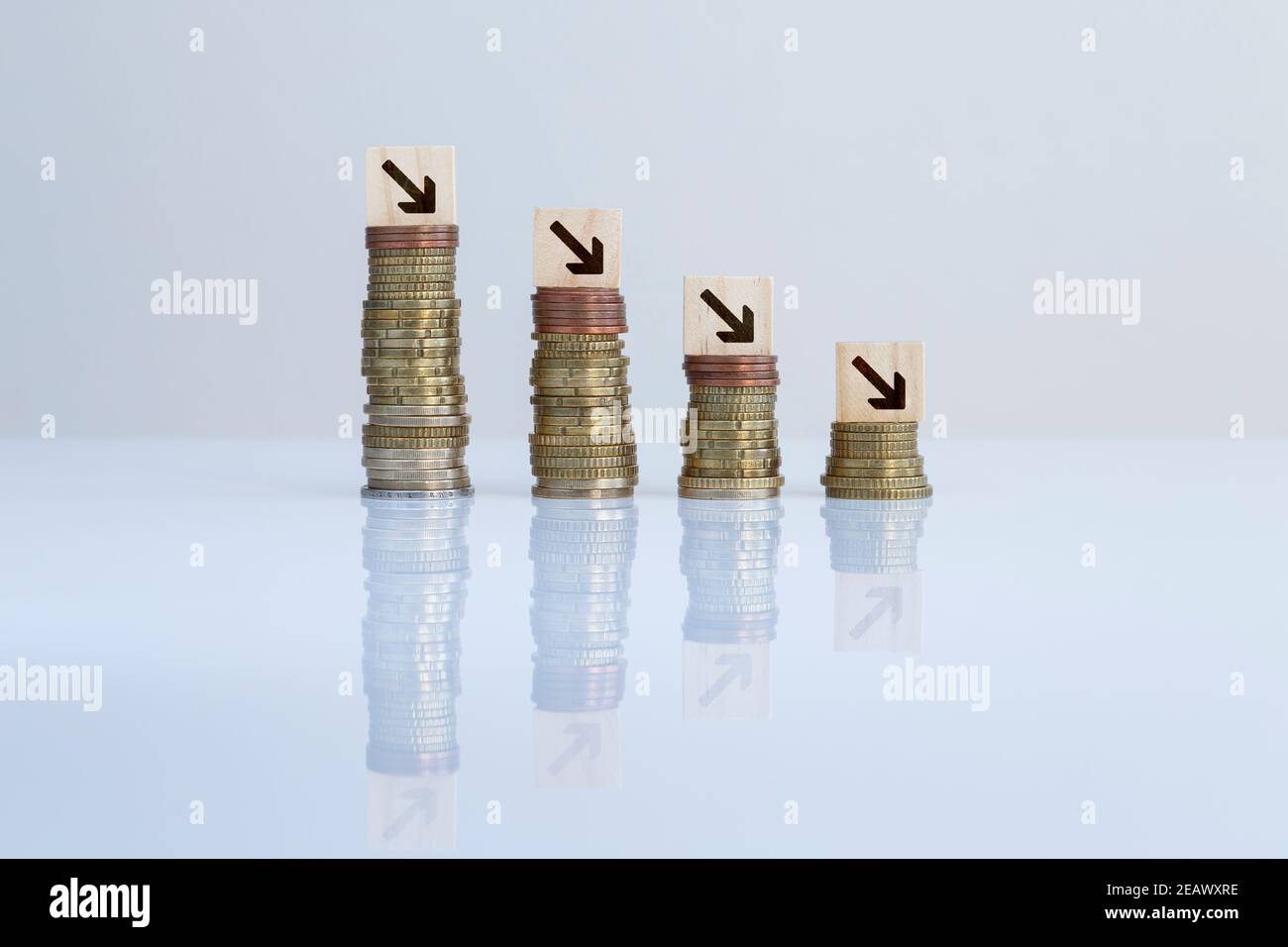 Pfeile auf Holzblöcken auf absteigenden Münzstapeln vor grauem Hintergrund. Konzept Foto von Wirtschaftskrise, Rezession, finanzielle Reduktion Stockfoto
