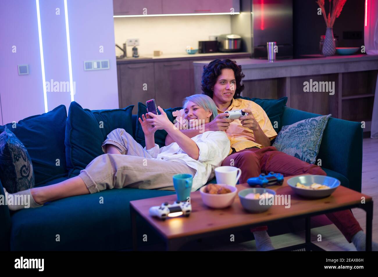 Glückliche junge Leute spielen Videospiele auf der Konsole, während sie auf der Couch vor dem fernseher sitzen. Millennial paar verbringen Spaß Zeit zusammen zu Hause. Zimmer Stockfoto