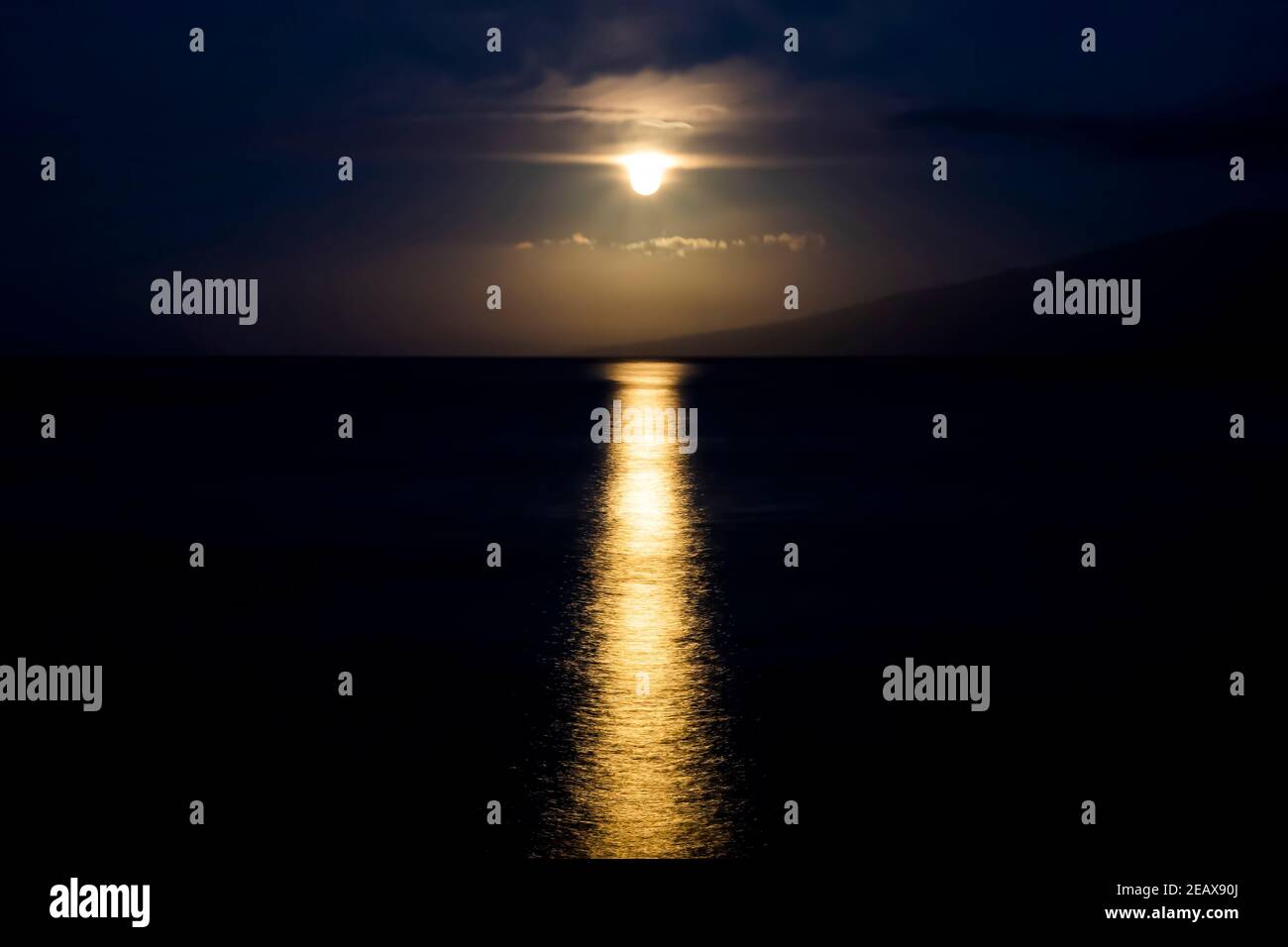 Vollmond, der durch Wolken untergeht, sieht so aus, als würde es mit Licht auf der Meeresoberfläche tropfen. Stockfoto