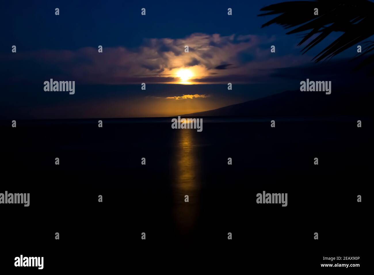 Vollmond über dem Ozean am frühen Morgen mit goldenem orangefarbenem Licht, das sich auf den Ozean im tropischen Hawaii reflektiert. Stockfoto