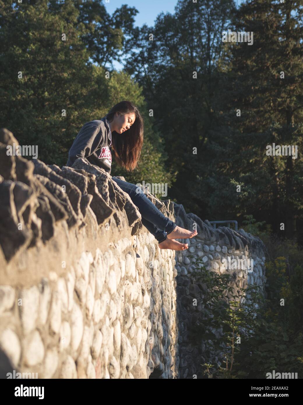 asiatische Mädchen sitzt auf einem Rock-Brücke Blick in die Entfernung an einem Bach mit Wald herum Stockfoto