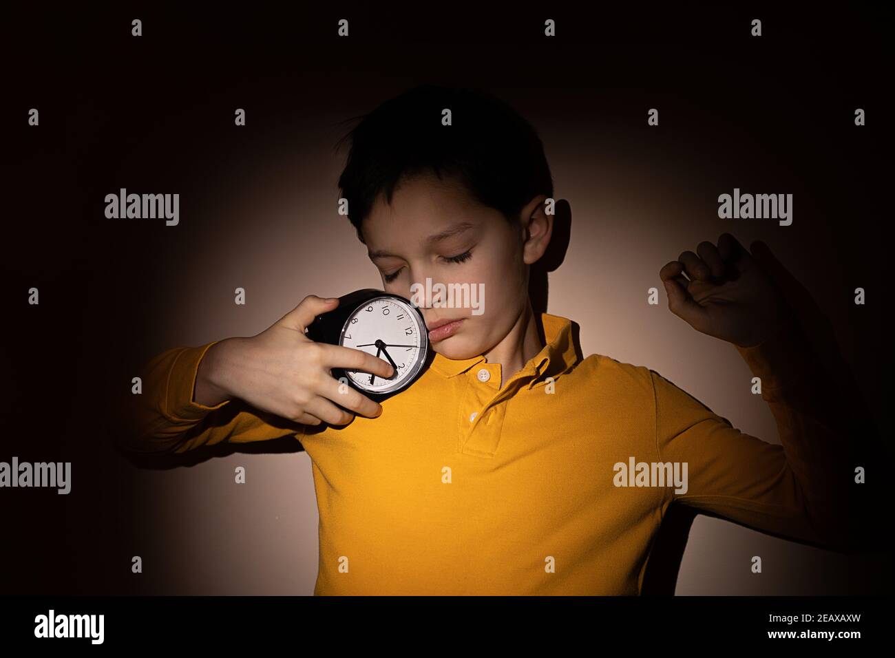 Teenager Junge hält Wecker in den Händen und schlafen unterwegs ein, Nacht. Konzept der Schlafstörung bei Kindern und Jugendlichen. Hartes Licht Stockfoto