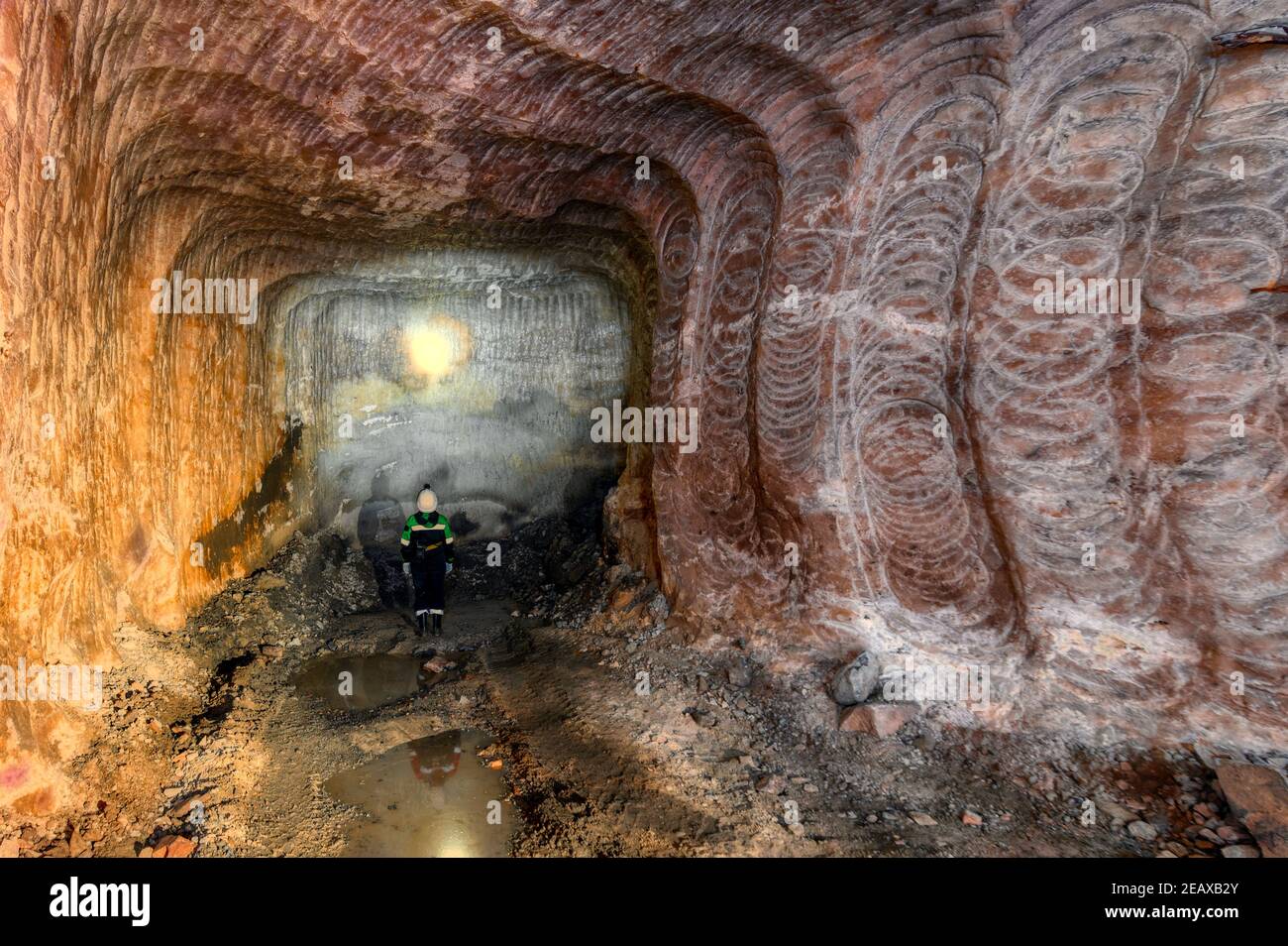 Ein Bergmann untersucht eine Mine und beleuchtet die Wände mit seiner Taschenlampe Stockfoto