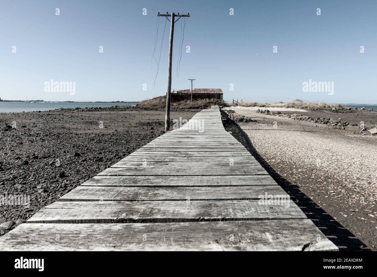 Rustikaler Holzweg führt zu alten Wasserscheide und Strommast mit geschnittenen Linien baumeln der Ocean Beach Road in Bluff Invercargill, Neuseeland. Stockfoto