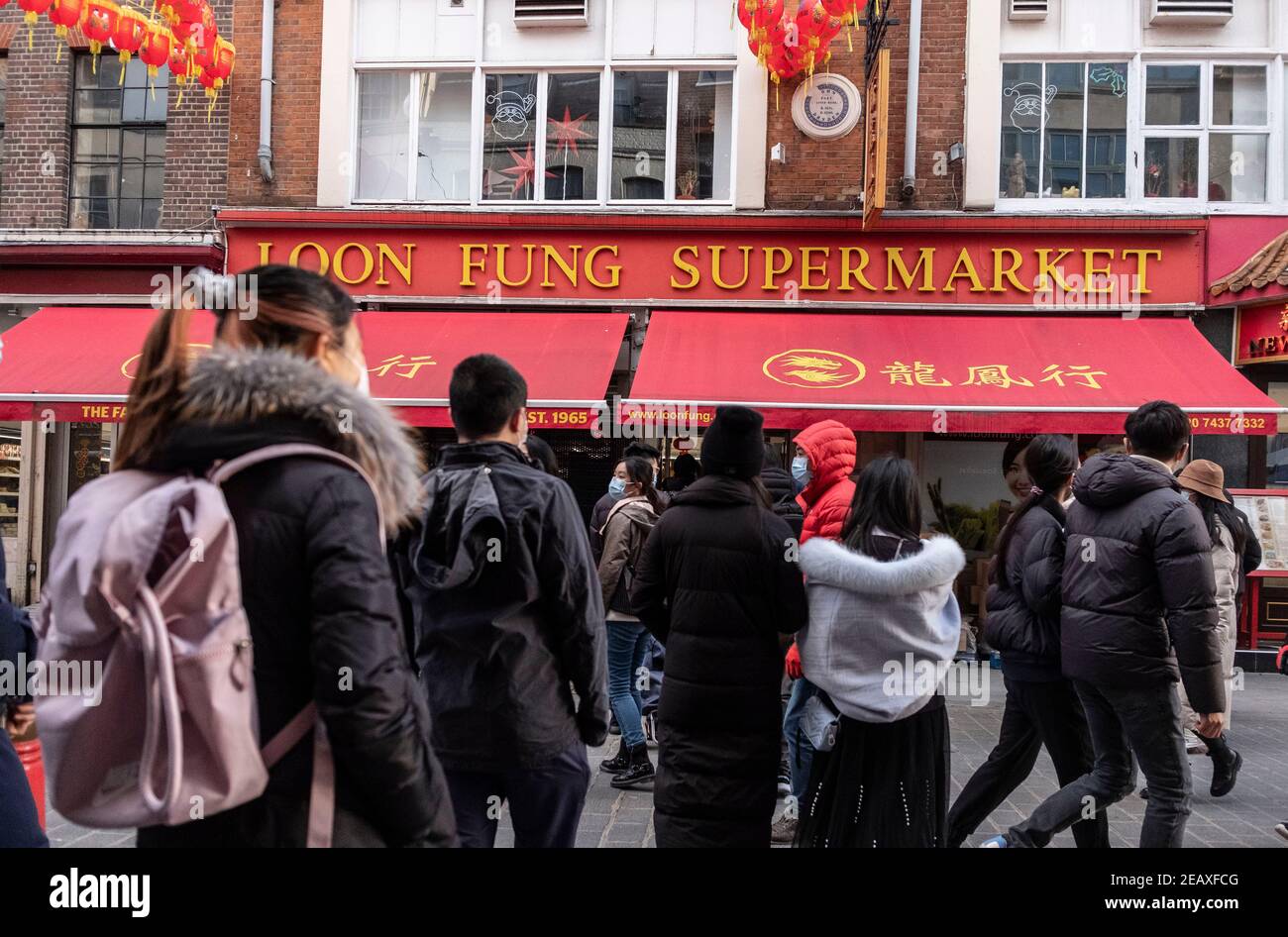 Menschen mit Gesichtsmasken als vorbeugende Maßnahme gegen die Ausbreitung der covid-19 Schlange vor chinesischen Shop in China Town, London.Chinese New Year ist das größte Festival in Asien. Jedes Jahr kommen Hunderttausende von Menschen ins Londoner West End, um eine farbenfrohe Parade, kostenlose Bühnenaufführungen und traditionelle chinesische Gerichte zu genießen und sich gegenseitig "Xin Nian Kuai Le" (auf Mandarin) oder "San Nin Faai Lok" (auf Kantonesisch) zu wünschen. Aufgrund nationaler Sperrbeschränkungen können die Menschen Londons chinesisches Neujahr von zu Hause aus mit einer Online-Feier der Vergangenheit C genießen Stockfoto