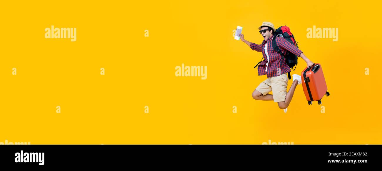 Attraktive glückliche junge asiatische Mann Tourist mit Flugticket und Pass springen isoliert auf gelbem Banner Hintergrund mit Copy Space Stockfoto