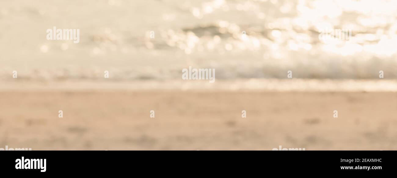 Verwischen Sie hellbraunen Sand und glitzerndes Meerwasser am Strand Im Sommer Banner-Hintergrund Stockfoto