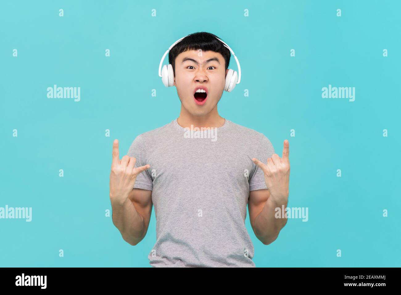 Cool Spaß asiatischen Mann trägt Kopfhörer und genießen zu hören Seine Lieblingssongs isoliert auf hellblauem Studiohintergrund Stockfoto