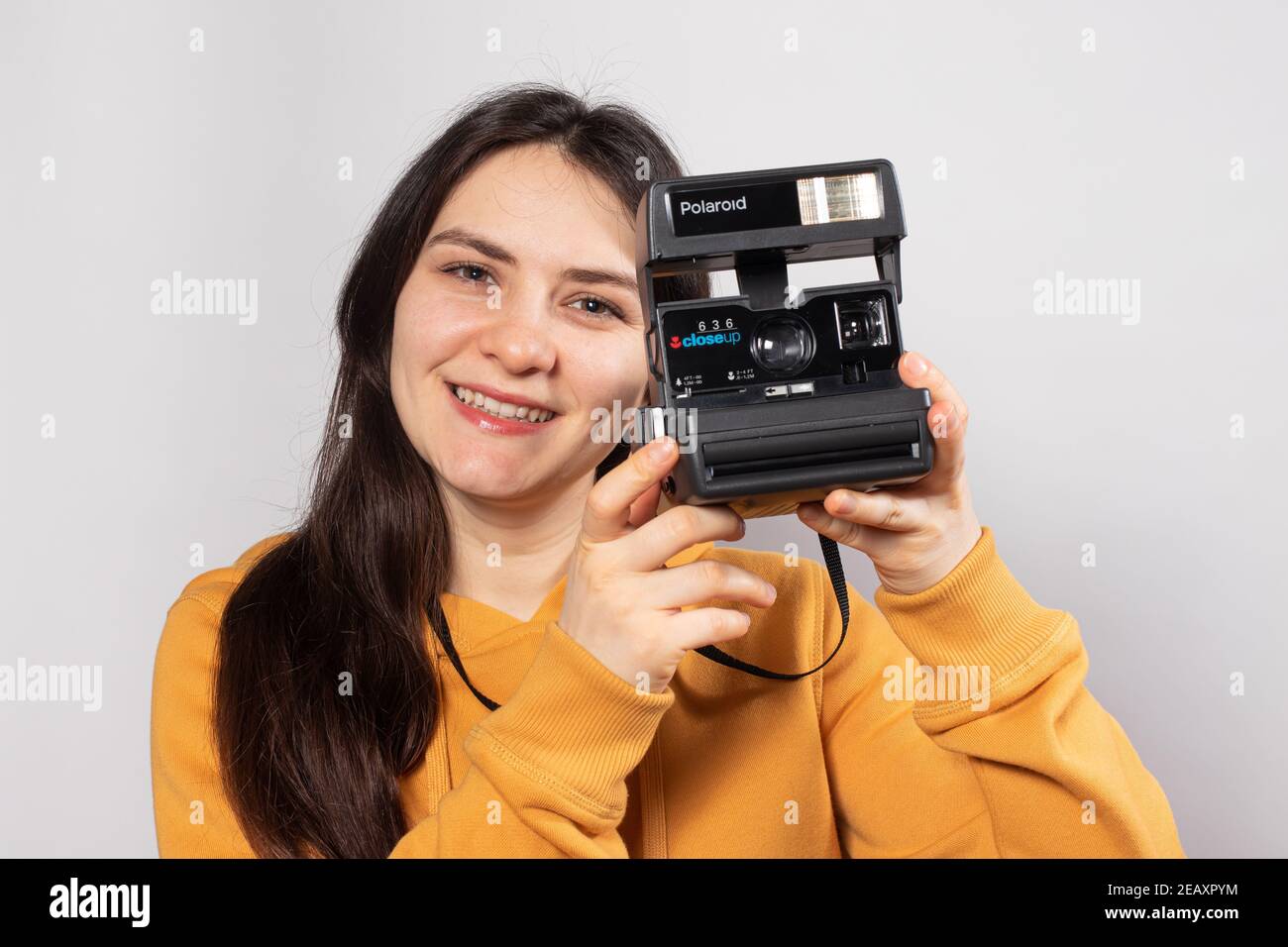 Eine schöne Brünette hält eine Polaroid-Kamera in der Hand und lächelt vor weißem Hintergrund. Fotografie Ausbildung, Fotografiekurse. Stockfoto