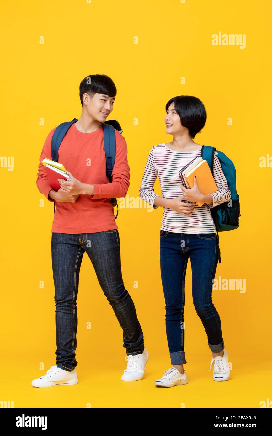 Energetische asiatische Studenten, die isoliert auf Gelb zusammen gehen und sprechen studio-Hintergrund Stockfoto