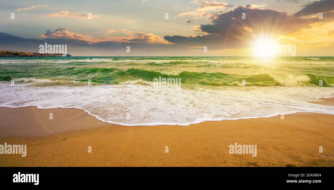 Meeresflut auf einem bewölkten Sonnenaufgang. Grüne Wellen krachenden goldenen Sandstrand im Morgenlicht. Sturmwetter nähert sich. Sommerferienkonzept Stockfoto