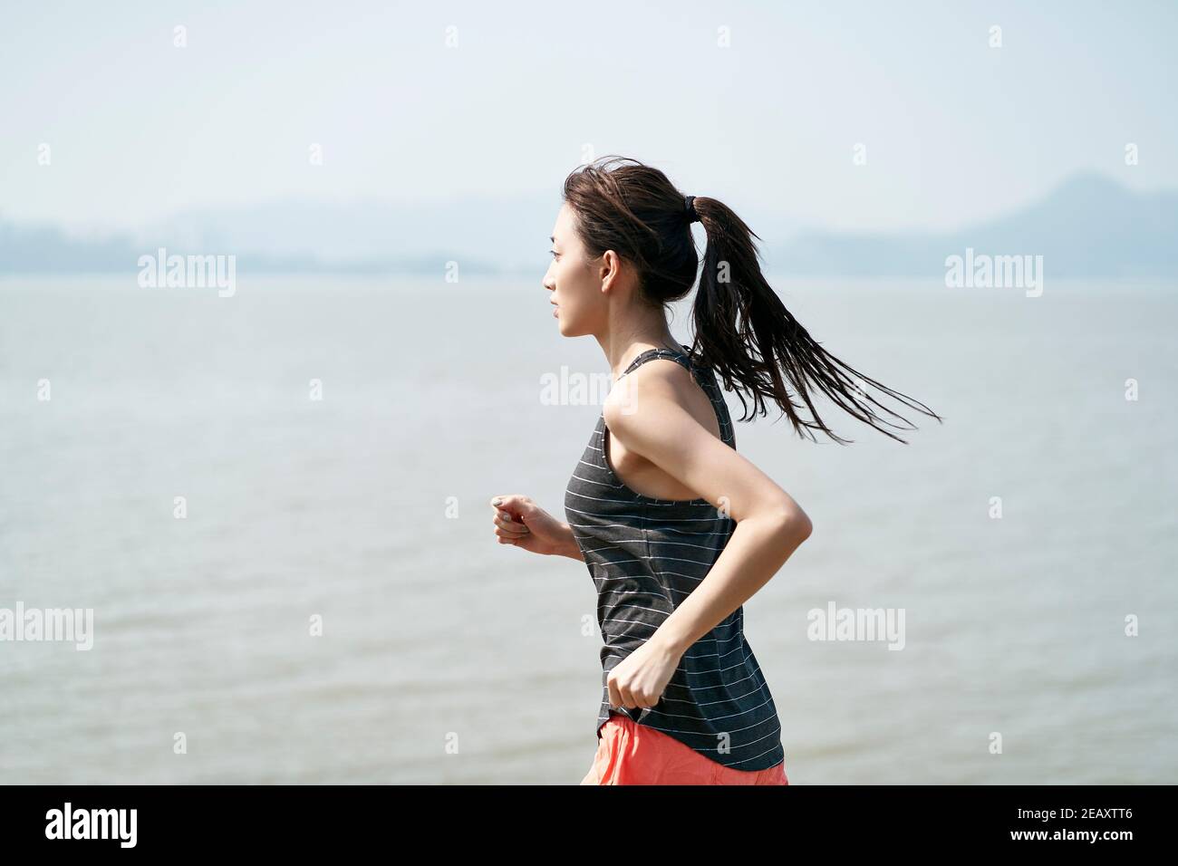 Junge asiatische Frau weibliche Läuferin läuft am Meer Stockfoto