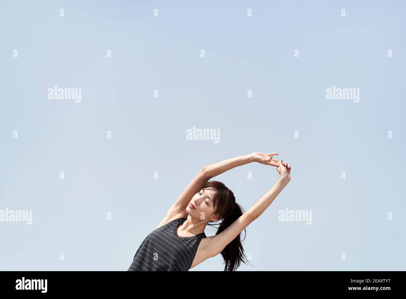 Junge asiatische Frau in Sportkleidung Stretching Arme im Freien gegen blau Himmel Stockfoto