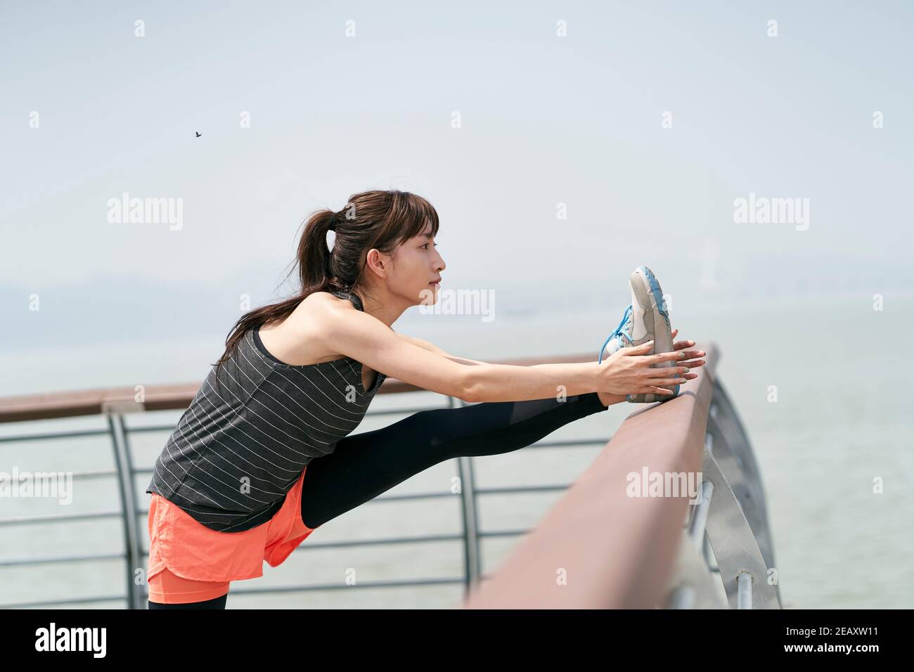 Junge asiatische Frau in Sportswear Stretching Beine im Freien in Meer parken Stockfoto